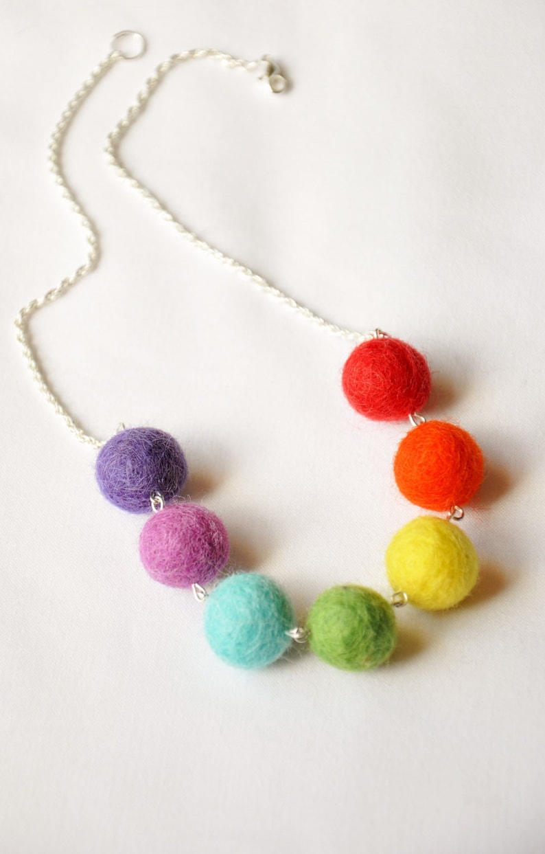 Puede incluir: Un collar de bolas de fieltro de colores arco&iacute;ris con una cadena plateada. Las bolas est&aacute;n en el orden de rojo, naranja, amarillo, verde, azul y morado.
