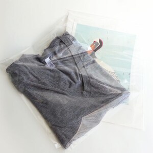 May include: A grey t-shirt folded and placed inside a clear plastic bag with a printed image of a bird.