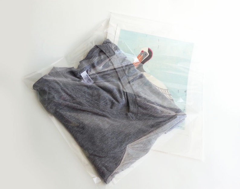 May include: A grey t-shirt folded and placed inside a clear plastic bag with a printed image of a bird.
