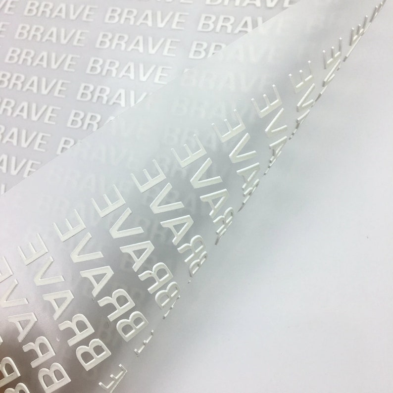 以下が含まれることがあります： 白い半透明シートのクローズアップ。シートには「BRAVE」という単語が繰り返しエンボス加工されています。