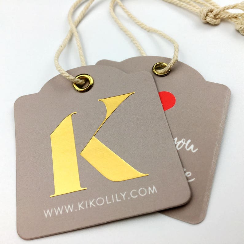 Pu&ograve; includere: Due etichette regalo in carta grigia con lettere dorate e bianche. L'etichetta pi&ugrave; grande ha una lettera K dorata e il testo "www.kikolily.com". L'etichetta pi&ugrave; piccola ha un cuore rosso e il testo "you".