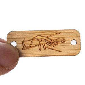 May include: A rectangular wooden tag with a laser-etched design of a lobster. The tag has two holes on the sides.