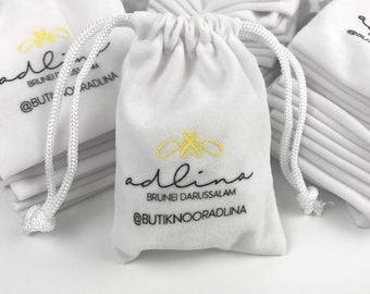 May include: White velvet drawstring bag with a gold bee logo and the text "adlina BRUNEI DARUSSALAM @BUTIKNOORADLINA".