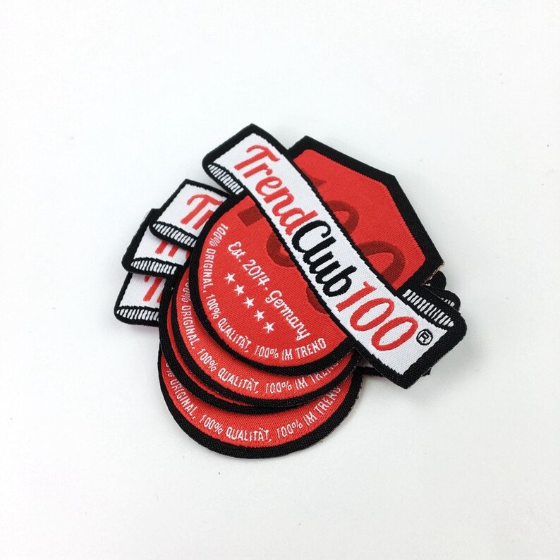 May include: A stack of red and white woven patches with black trim. The patches feature the text "Trend Club 100" and "Est. 2014 - Germany".
