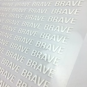 以下が含まれることがあります： 白いビニールシートのクローズアップ。シートには「BRAVE」という単語が斜めに複数回繰り返されています。