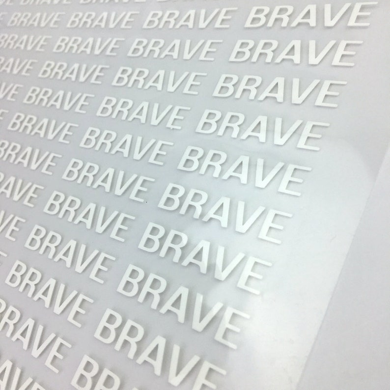 以下が含まれることがあります： 白いビニールシートのクローズアップ。シートには「BRAVE」という単語が斜めに複数回繰り返されています。