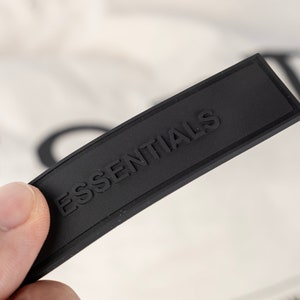 May include: A black rectangular tag with the word "ESSENTIALS" embossed in white lettering.
