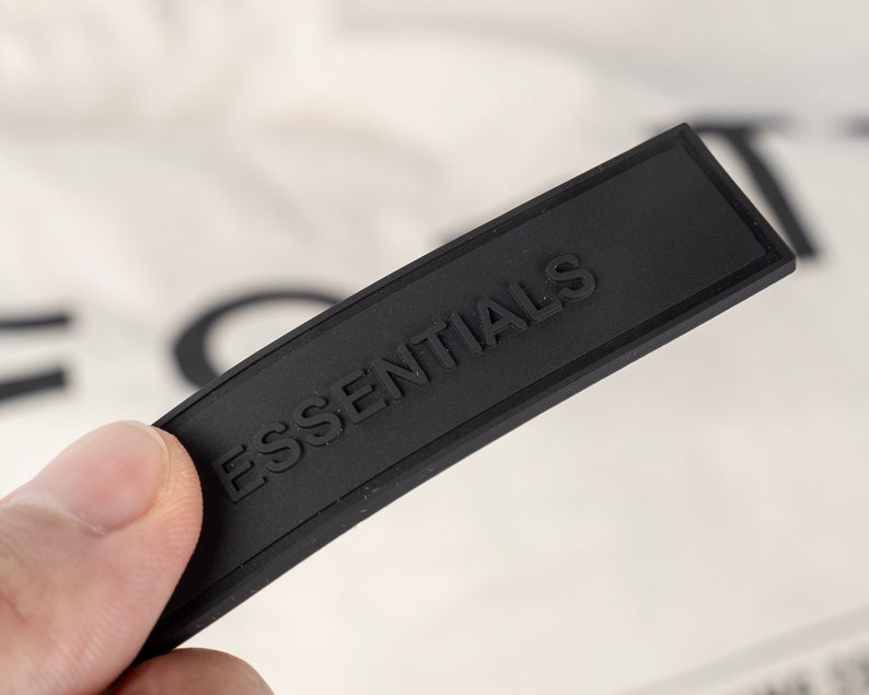 May include: A black rectangular tag with the word "ESSENTIALS" embossed in white lettering.