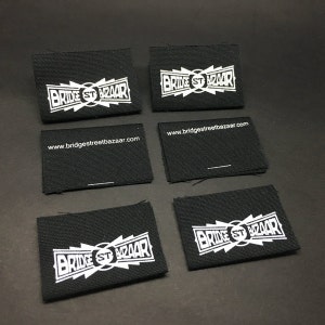 May include: Six black fabric labels with white text. The text on the labels reads "Bridge St Bazaar" and "www.bridgestreetbazaar.com".