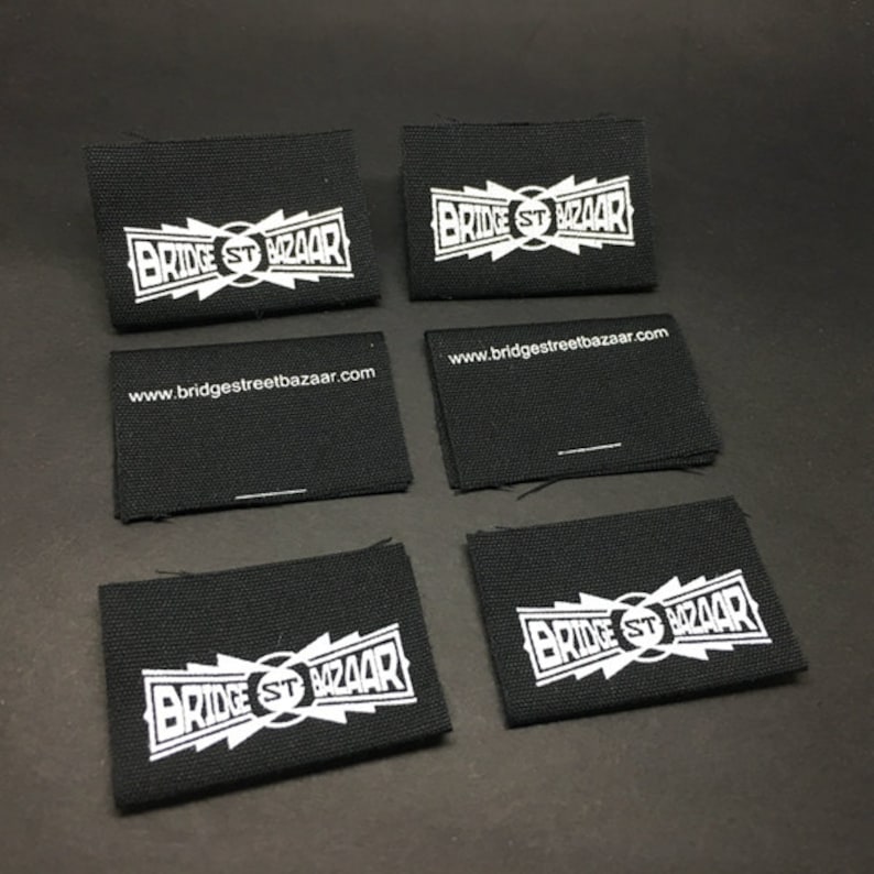 May include: Six black fabric labels with white text. The text on the labels reads "Bridge St Bazaar" and "www.bridgestreetbazaar.com".