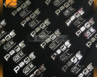 May include: Close-up of a black fabric with silver foil labels that say "Page One" with different size options. The labels are embossed and have a shiny finish.