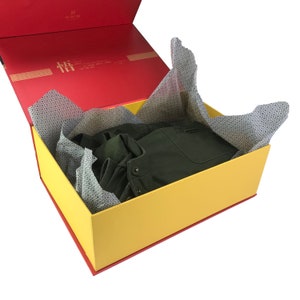 May include: A yellow and red gift box with a green jacket inside. The box is lined with white tissue paper with a black and white pattern.