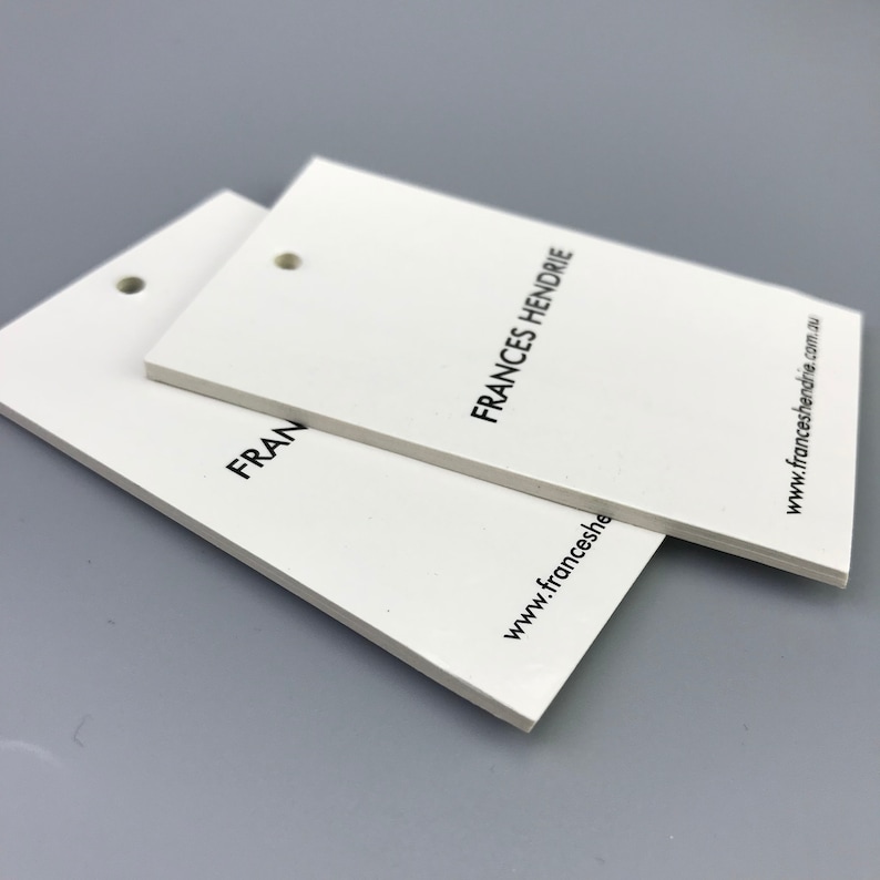 May include: Two white rectangular hang tags with rounded corners and a hole punched in the top left corner. The top tag has the text "FRANCES HENDRIE" printed in black. The bottom tag has the text "FRAN" printed in black. The text "www.franceshendrie.com.au" is printed in black on the right side of the top tag.