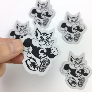 May include: Five black and white iron-on patches of a cartoon cat wearing a jersey with a letter C on it. The cat is running and has an angry expression.