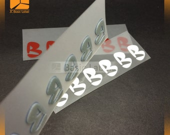 May include: A close-up of two sheets of clear adhesive paper with rows of white and blue 3D letters that spell out "Basic Label". The letters are raised and have a textured surface.