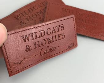 May include: Three brown leather patches with the text "Wildcats & Homies - Collabo" embossed on them.