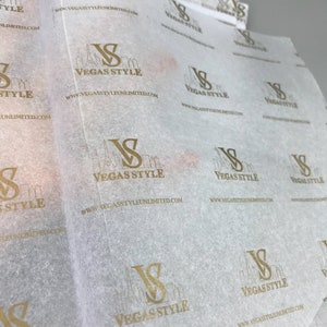 以下が含まれることがあります： 「Vegas Style」とスタイリッシュな街並み、ウェブサイト「www.vegasstyleunlimited.com」が書かれた金色のロゴが繰り返しパターン化された白いティッシュペーパーです。