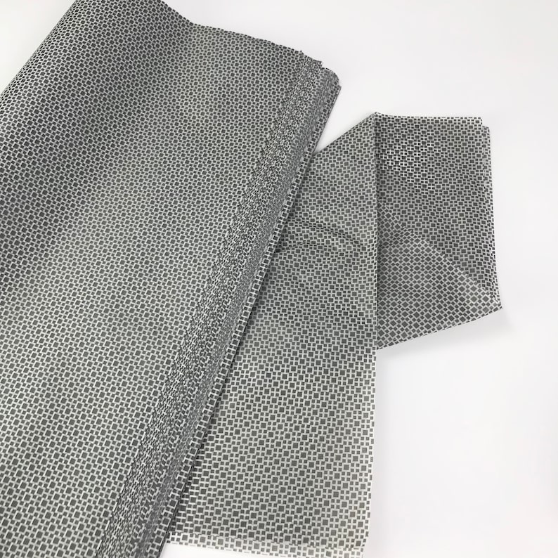 May include: A stack of gray tissue paper with a small geometric pattern. The tissue paper is folded and arranged in a rectangular shape.