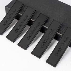 May include: Five black rectangular fabric patches with the word "ESSENTIALS" embossed in white lettering.