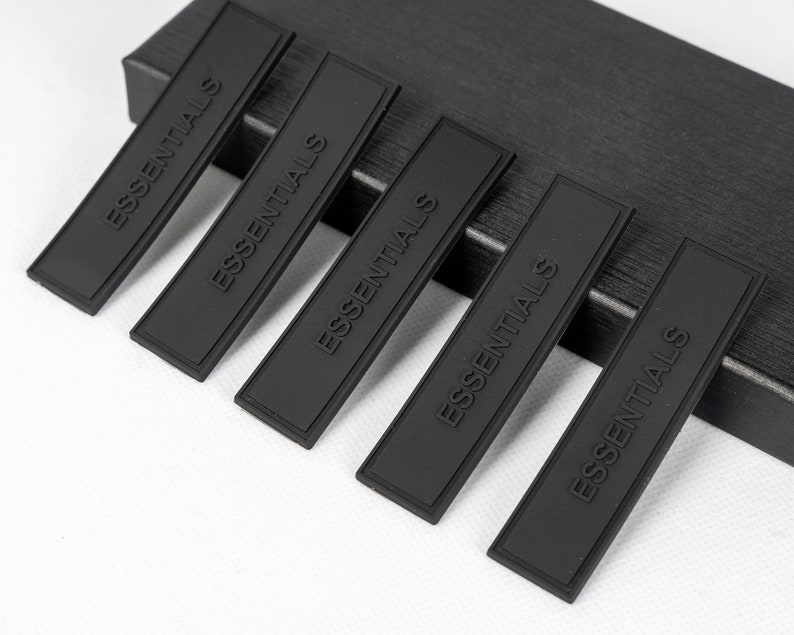 May include: Five black rectangular fabric patches with the word "ESSENTIALS" embossed in white lettering.