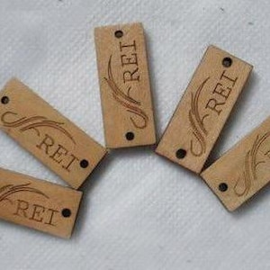 May include: Five wooden tags with the word "REI" engraved on them. Each tag has a decorative design with a stylized swirl.