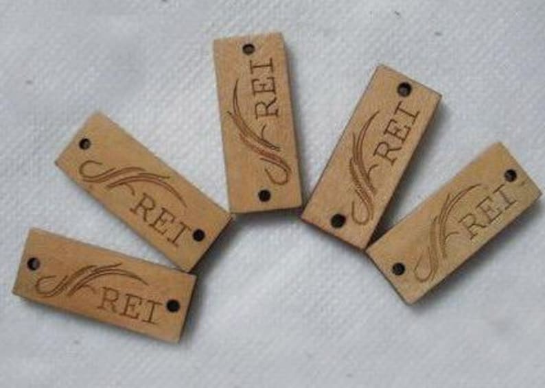 May include: Five wooden tags with the word "REI" engraved on them. Each tag has a decorative design with a stylized swirl.