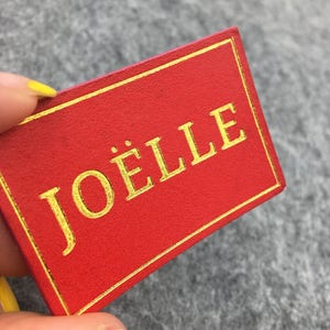 May include: A red rectangular tag with a gold border and the word "JOËLLE" written in gold lettering.
