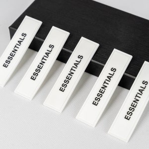 May include: Five white rectangular labels with the word "ESSENTIALS" printed in black on each label. The labels are arranged in a row, with the top label slightly offset to the left.