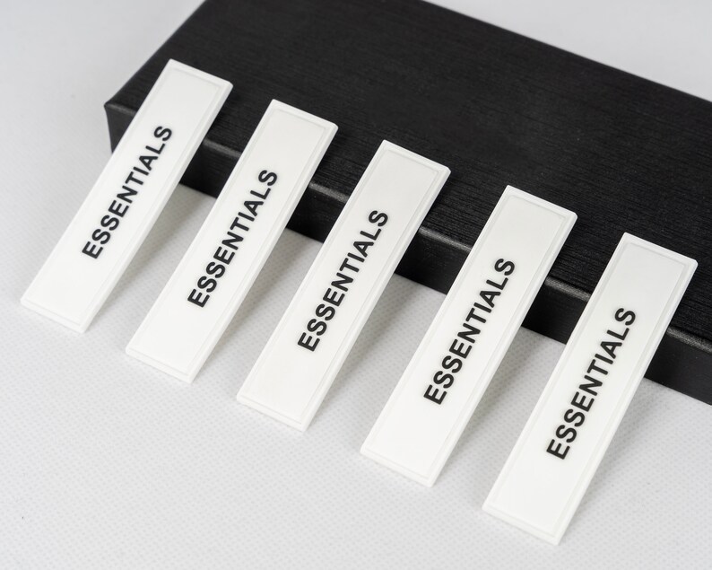 May include: Five white rectangular labels with the word "ESSENTIALS" printed in black on each label. The labels are arranged in a row, with the top label slightly offset to the left.