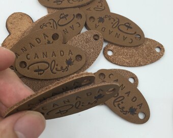 May include: A pile of brown leather oval-shaped tags with the text "CANADA Bliss" engraved on them.