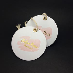 Pu&ograve; includere: Due etichette regalo rotonde bianche con scritta dorata. L'etichetta superiore dice "Rose" e l'etichetta inferiore dice "Sofia Rose Boutique". Entrambe le etichette hanno un design ad acquerello rosa e un occhiello dorato.