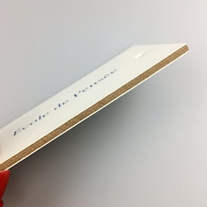 May include: A white card with the text "Ecole de pensee" printed in blue ink. The card is made of thick paper with a brown cardboard backing.