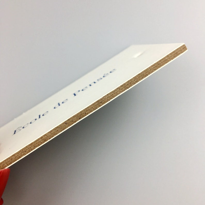 May include: A white card with the text "Ecole de pensee" printed in blue ink. The card is made of thick paper with a brown cardboard backing.