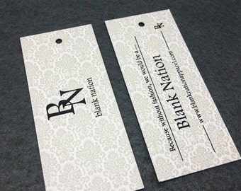 May include: Two white rectangular hang tags with a black damask pattern. The tag on the left has the letters "BN" in black. The tag on the right has the text "Because without fashion, we would be a... Blank Nation www.blanknationapparel.com" in black.