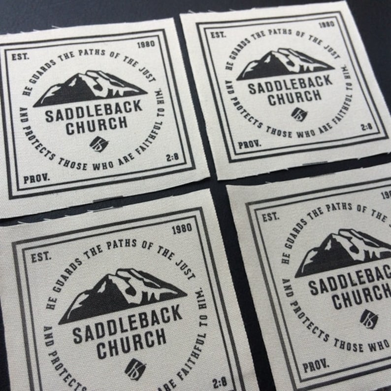 May include: Four beige fabric patches with black text and a mountain graphic. The text reads "EST. 1980 HE GUARDS THE PATHS OF THE JUST AND PROTECTS THOSE WHO ARE FAITHFUL TO HIM. SADDLEBACK CHURCH PROV. 2:8".