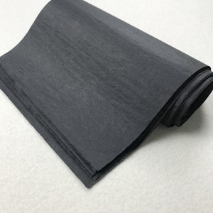 May include: A roll of black tissue paper. The paper is folded and rolled up, showing the texture of the paper.