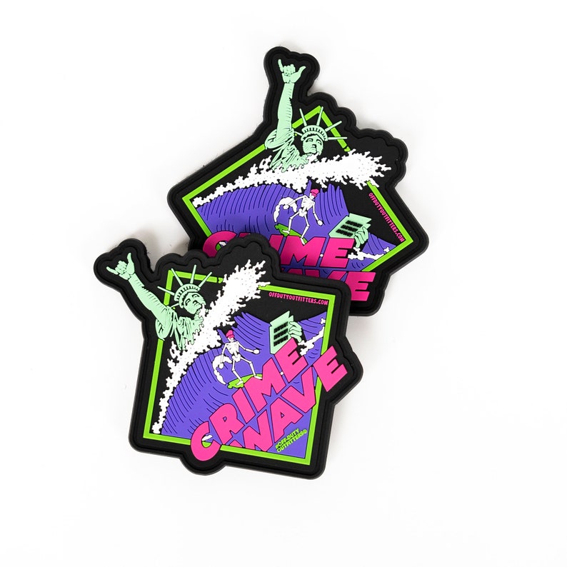 May include: Two black, square stickers with a graphic design. The design features the Statue of Liberty riding a wave, with the words "CRIME WAVE" in pink and the website address "OFFDUTYSTICKERS.COM". The background is purple and green.