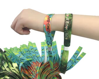 May include: A stack of colorful wristbands with the text "Garden of Eden" and "b YOUNG-BAETE" printed on them. The wristbands are made of woven fabric and have a metal clasp.