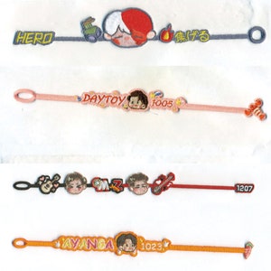 May include: Embroidered fabric bracelets in various colours. One bracelet has the word "HERO" and a cartoon character. Another has "DAYTOY" and "1005". The third has "CMZ" and "1207". The last has "AYANGA" and "1023".