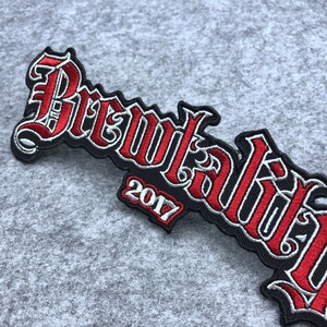 May include: Red and silver embroidered patch with the text "Brewtaliti" and the year "2017" in a black font.
