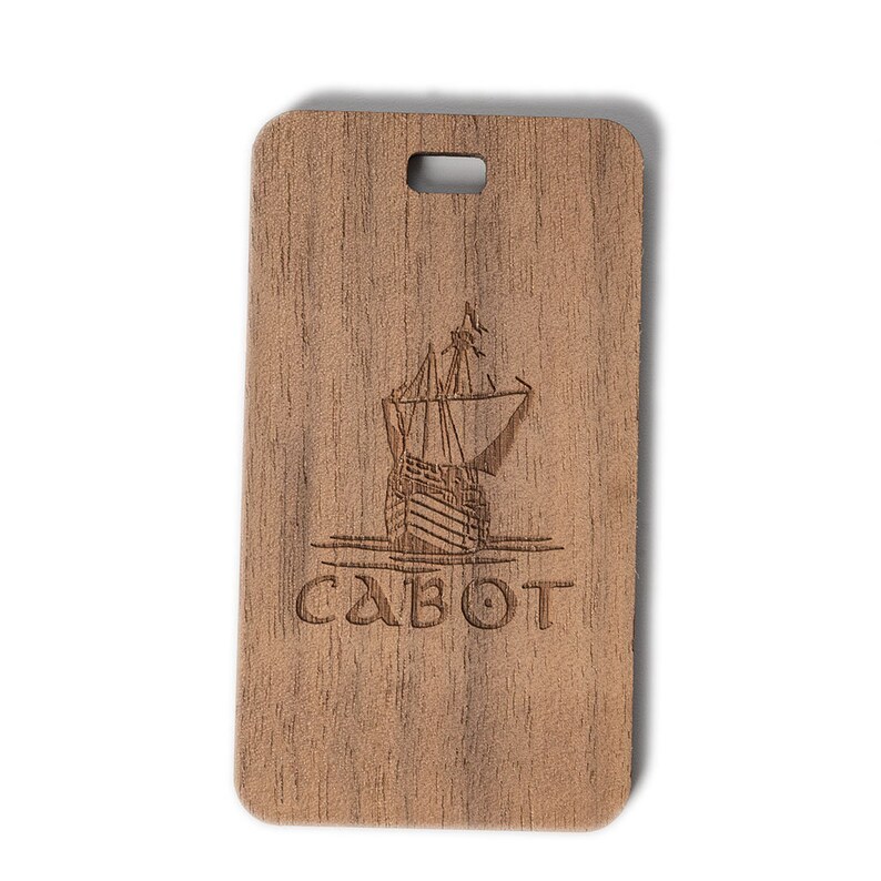 May include: A wooden luggage tag with a laser-engraved image of a ship and the word "CABOT".