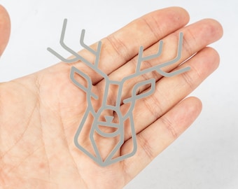 May include: A silver geometric deer head design, outlined in a thin line, is held in a person's hand.