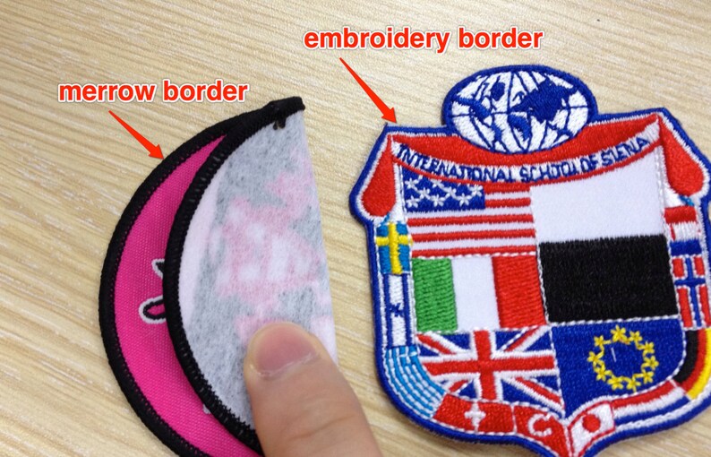 May include: Two embroidered patches, one with a circular merrow border and the other with an embroidered border. The circular patch is pink and white with a black merrow border. The other patch is a shield shape with a red, white, and blue embroidered border. The shield has a globe with a blue outline and the text "INTERNATIONAL SCHOOL OF SIENA" in a blue arc above the globe. The shield is divided into sections with different flags embroidered on each section.