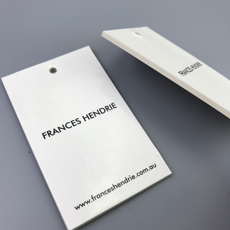 May include: Two white rectangular hang tags with rounded corners and a hole punched in the top. The tag on the left has the text "FRANCES HENDRIE" printed in black and the text "www.franceshendrie.com.au" printed in black below. The tag on the right has the text "FRANCES HENDRIE" printed in black.