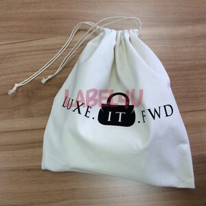 May include: White cotton drawstring bag with black text and a black silhouette of a handbag. The text reads "LUXE. IT. FWD"