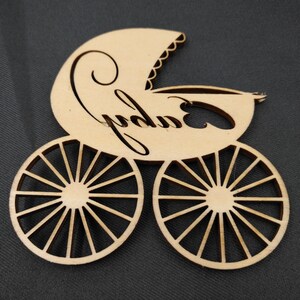 May include: Wooden cutout of a baby carriage with the word "baby" written on it. The carriage has wheels with spokes.