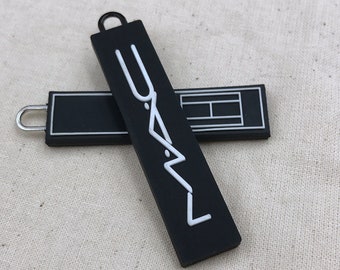 May include: Black zipper pull with a white "MAC" logo. The zipper pull is made of rubber and has a small loop at the top.