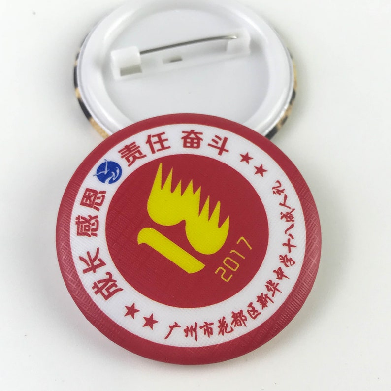 Może przedstawiać: Czerwono-biały guzik z ż&oacute;łtym wzorem płomienia i chińskim tekstem. Tekst brzmi "Guangzhou New Color Printing Factory" i "2017".