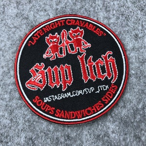 May include: A black and red embroidered patch with the text "Late Night Cravables" and "Sup Itch" in a gothic font. The patch also features two red cartoon devils and the text "Soups Sandwiches Sides" and "Instagram.com/sup_itch".