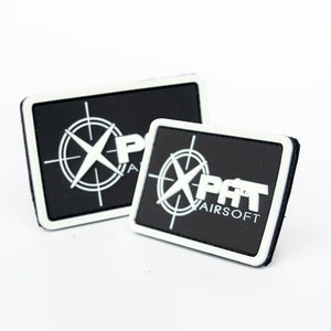 May include: Two black and white rectangular patches. Each patch features a white compass design with the text "X PAT AIRSOFT". The patches have a white border and are set against a white background.